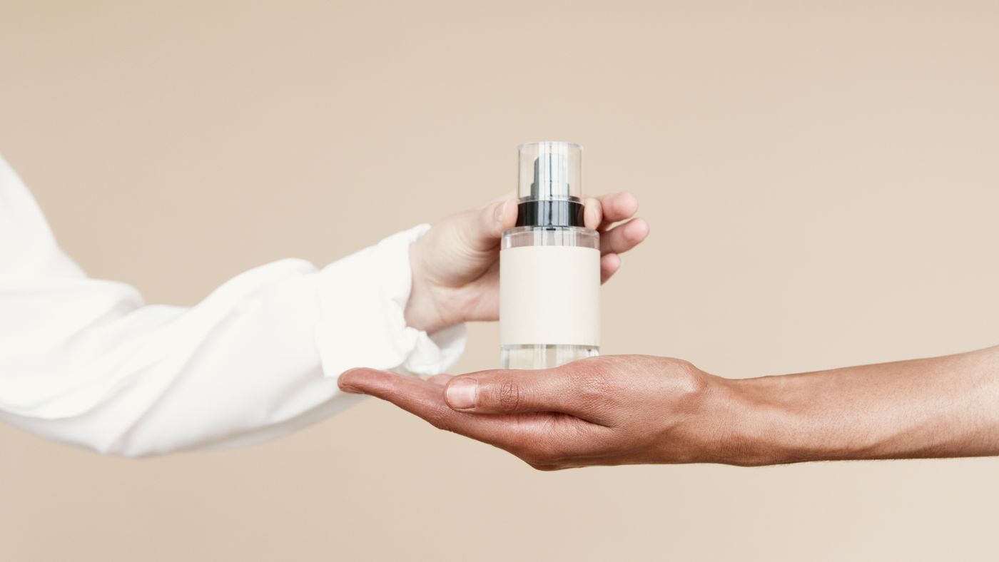 Two hands sharing a bottle of face oil